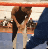 a man in a black tank top is standing in a boxing ring holding his pants up