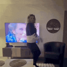 a woman is dancing in front of a television which says 21:10 on it