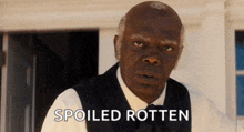 a man in a suit stands in front of a sign that reads spoiled rotten