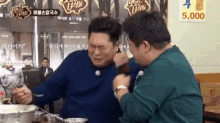 two men are sitting at a table with a bowl of food and a sign that says 5,000 on it .