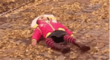 a little girl in a red jacket is laying on the ground covered in leaves .