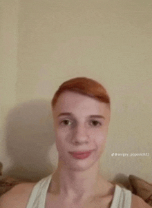 a young man with red hair is wearing a white tank top and smiling .