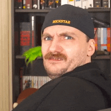 a man with a mustache wearing a black hat that says rockstar on it .