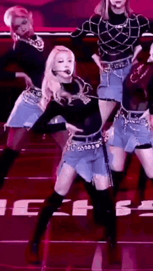 a group of women are dancing on a stage in front of a pink background .