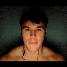 a shirtless man wearing headphones is looking at the camera in a dark room .