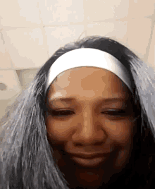 a woman with gray hair and a white headband smiles for the camera