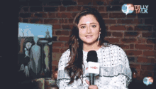 a woman is holding a microphone in front of a brick wall that says telly talk on it