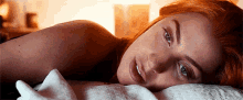 a woman with red hair is laying on a bed with a white blanket .