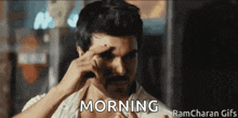a man with a mustache is holding his hand to his forehead and the word morning is written on the screen .