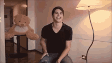 a man is sitting in front of a teddy bear and smiling