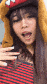 a woman wearing a striped shirt and a hat with a dinosaur on it is making a funny face .