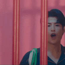a man in a blue shirt is peeking out from behind a fence .