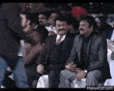 a group of men in suits and ties are sitting in a stadium laughing .