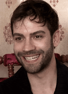 a man with a beard is smiling with a floral wallpaper in the background