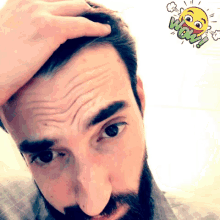 a man with a beard holds his hand to his forehead with a cartoon smiley face that says wow behind him
