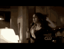 a woman is standing in a dark room holding a bottle of wine and her hair is being blow dried .