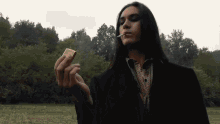 a man with long hair is smoking a cigarette outdoors