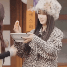 a woman in a leopard print jacket is holding a bowl of food in her hand .