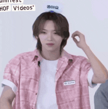 a young man wearing a pink plaid shirt and a white t-shirt is holding his head .