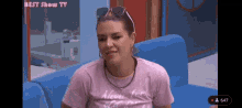 a woman is sitting on a blue couch wearing sunglasses and a pink shirt that says never from