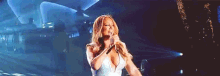 mariah carey is singing into a microphone on a stage .