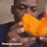 a man is eating a slice of mango with the hashtag #mangoseason on the bottom