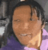 a close up of a person 's face with a purple shirt on and a smile on their face .