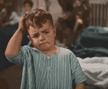 a little boy is scratching his head while wearing a blue striped shirt .