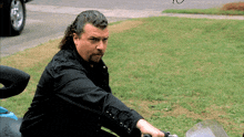 a man in a black shirt sits on a motorcycle in the grass