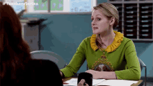 a woman in a green sweater is sitting at a desk with a cup of coffee .