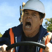 a man wearing a hard hat and safety vest is driving a vehicle with his mouth open