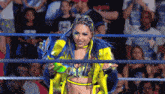 a woman in a yellow and blue outfit is standing in a wrestling ring in front of a crowd .