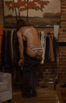 a woman in a bikini is putting on her pants in a room with a brick wall .