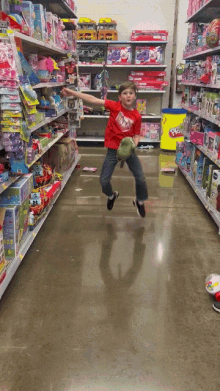 a young boy in a red shirt is jumping in the air in a toy store