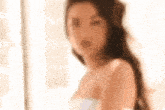 a woman in a white dress is standing in front of a window and looking at the camera .