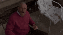 a bald man in a red sweater and glasses is sitting at a table with his mouth open .