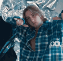 a young man wearing a blue plaid shirt is pointing at the camera .