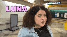 a woman with curly hair stands in front of a sign that says luna on it