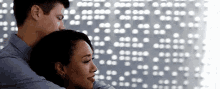 a man and a woman are hugging each other in front of a white wall .
