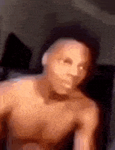 a man without a shirt is sitting on a couch and making a funny face .