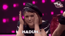 a woman wearing a beret is covering her face with her hands and says haduh .