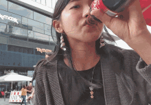 a woman drinking from a coca cola bottle in front of a knick knack store
