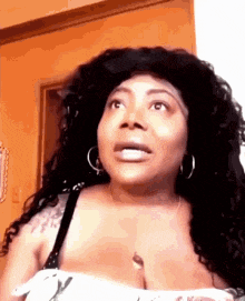a woman with long curly hair is making a funny face while wearing a bra and earrings .