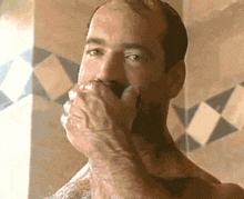 a shirtless man covering his mouth with his hand in a bathroom