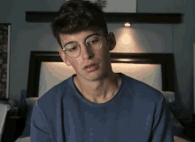 a young man wearing glasses and a blue shirt looks at the camera