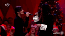 two women singing in front of a christmas tree with a tv8 logo in the corner