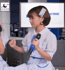 a girl in a white dress is holding a microphone in front of a sign that says honeycam