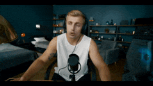 a man wearing headphones and a white tank top talks into a microphone
