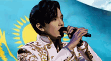 a man is singing into a microphone in front of a blue and yellow flag