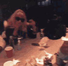 a woman in sunglasses sits at a table with a red cup